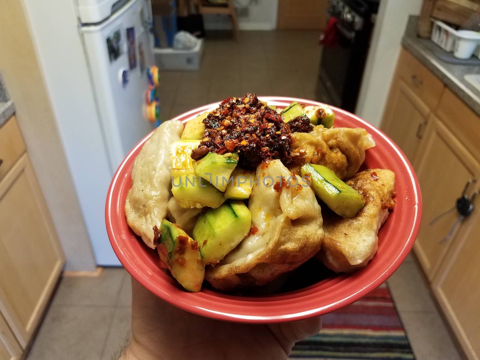 hand holding red bowl with Chinese dumplings and cucumber and chili sauce