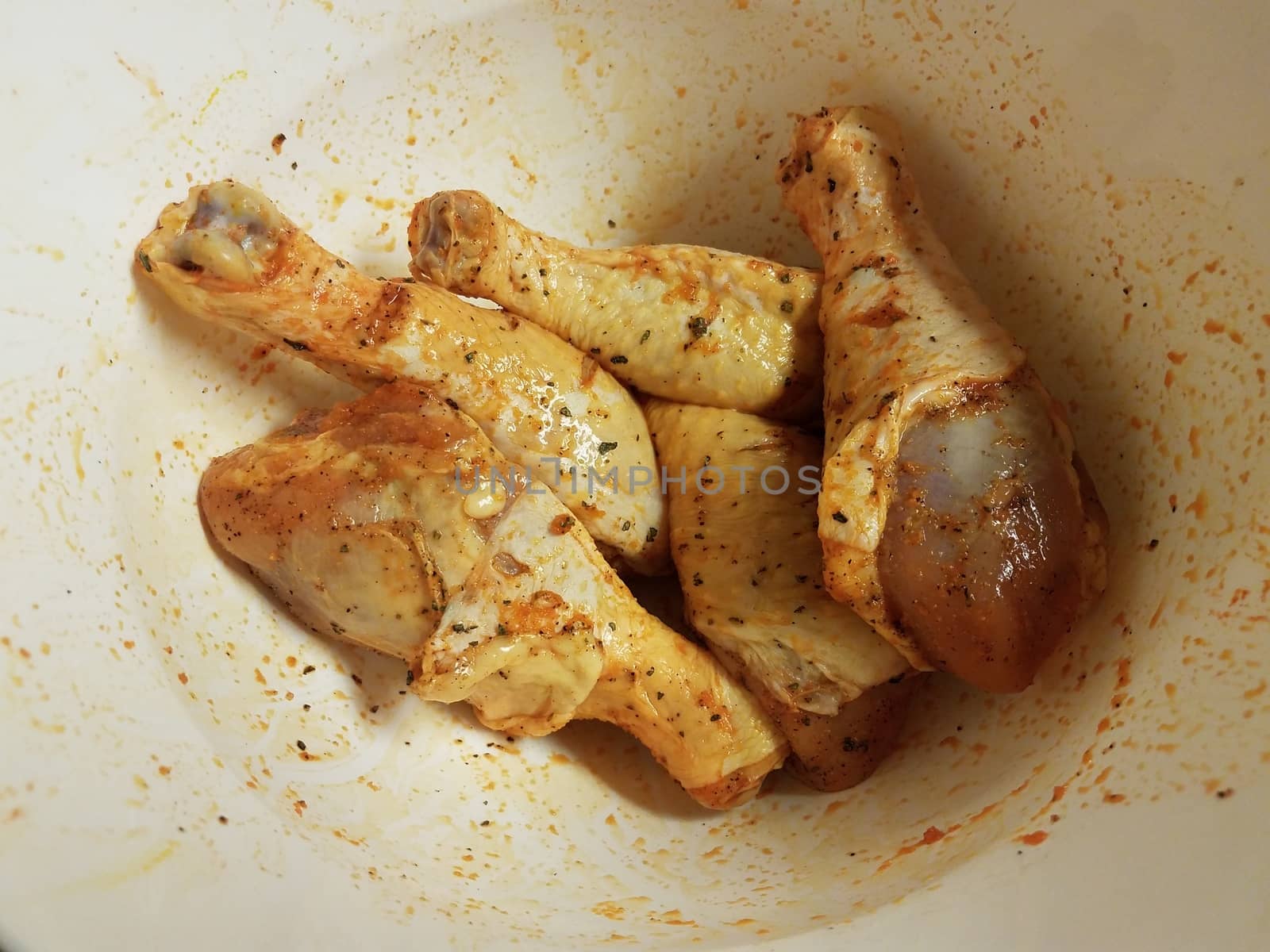 seasoned raw chicken drumsticks or poultry in white bowl