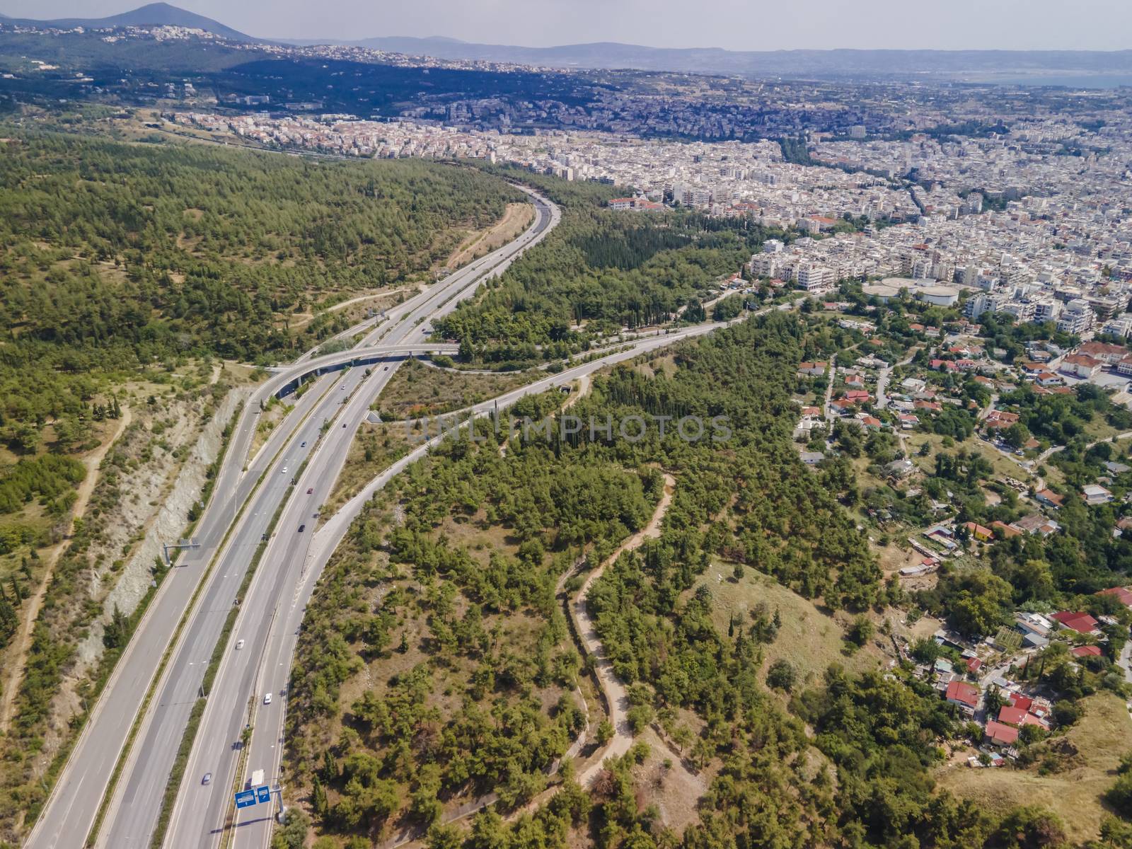 Day top panorama of European highway with passing cars through forest on city outskirts.