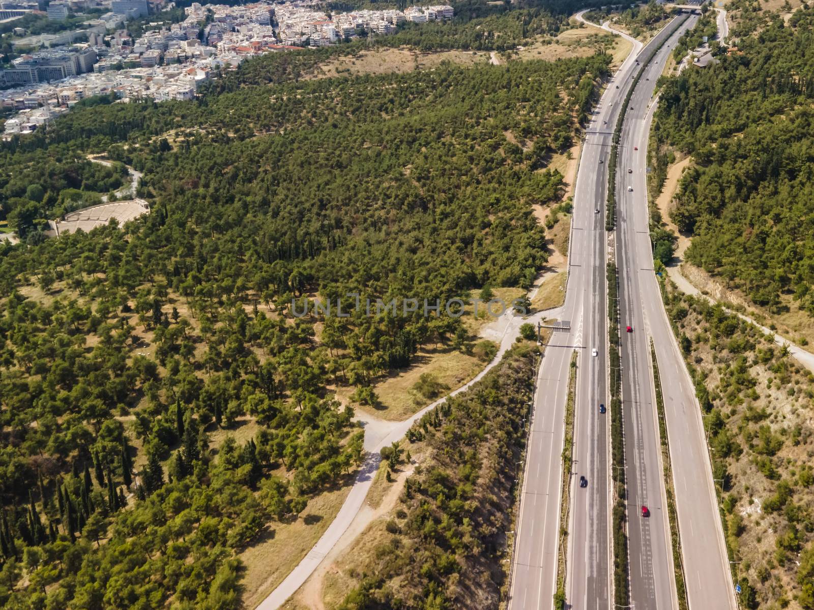 Day top panorama of European highway with passing cars through forest on city outskirts.