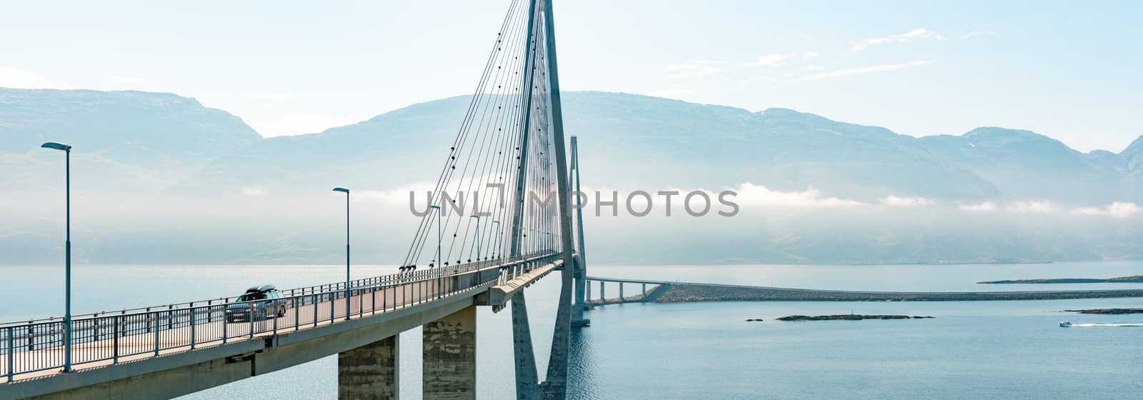 Panorama of car on road in Norway, Europe. Auto travel through scandinavia. Blue cloudy sky, lake and bridge in background.