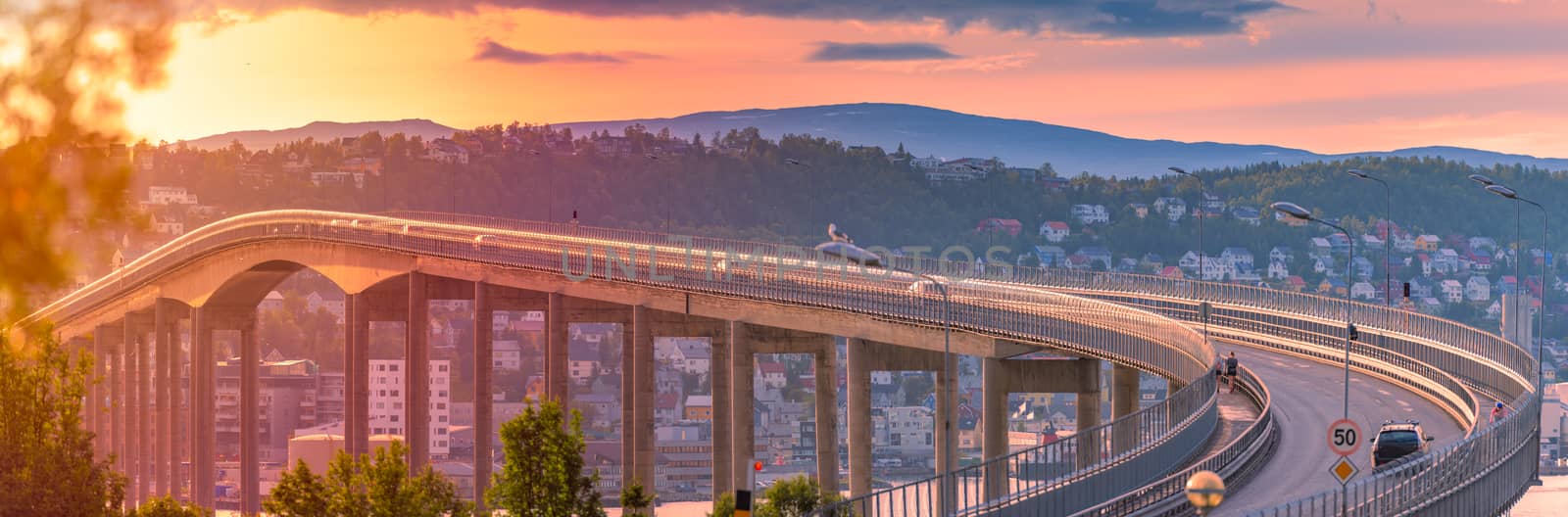 Panorama of bridge in Tromso and car road in Norway, Europe. Auto travel through scandinavia. Sunset with mountain and clouds in background.