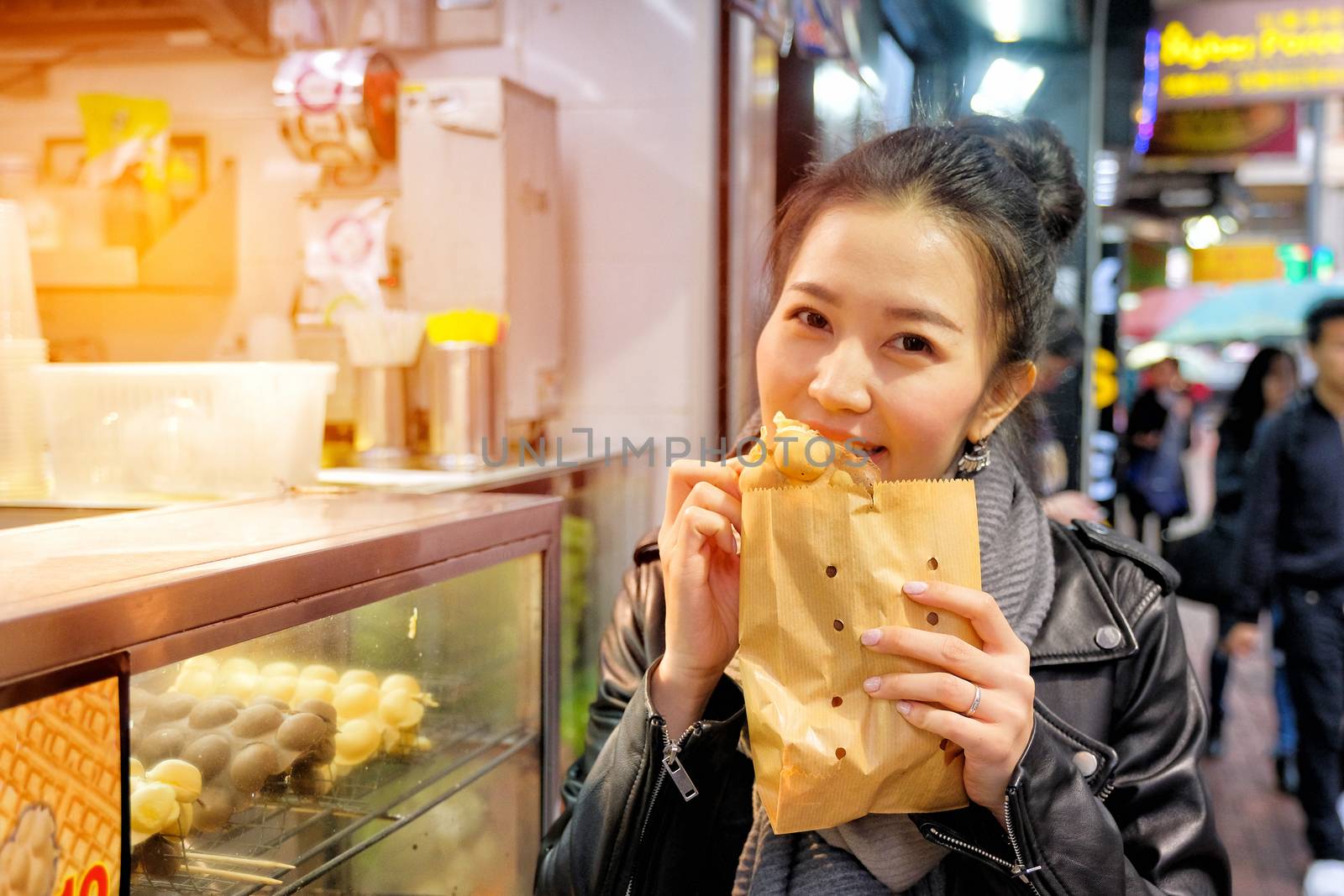 Young woman eating waffle street food in hong kong by Surasak