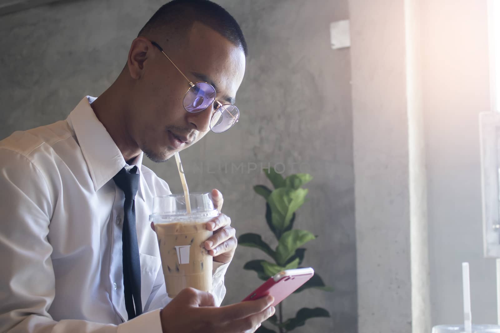 Young business man drinking ice coffee and using phone