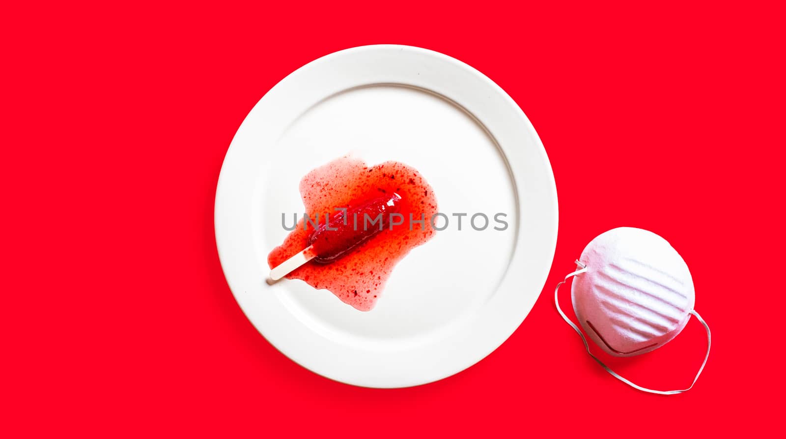 Delicious defrosted strawberry popsicles and medical mask over red background