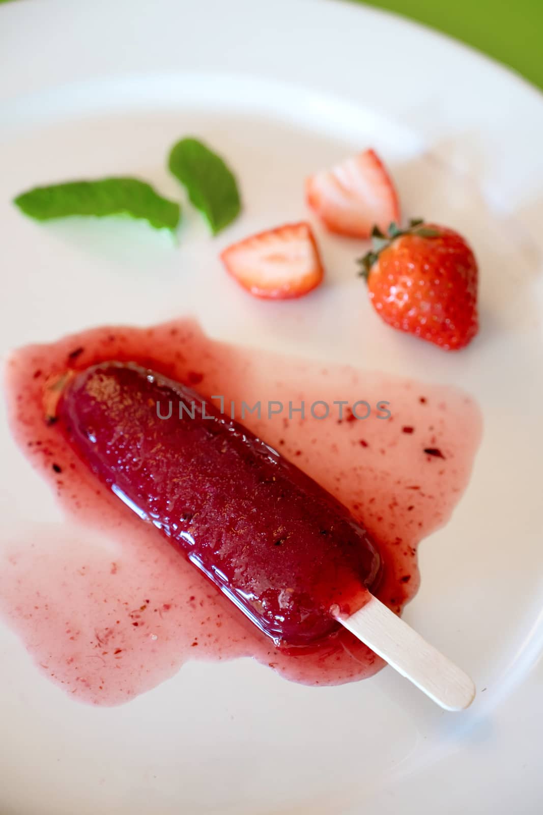 Delicious defrosted strawberry popsicle on white round dish over green background by raferto1973