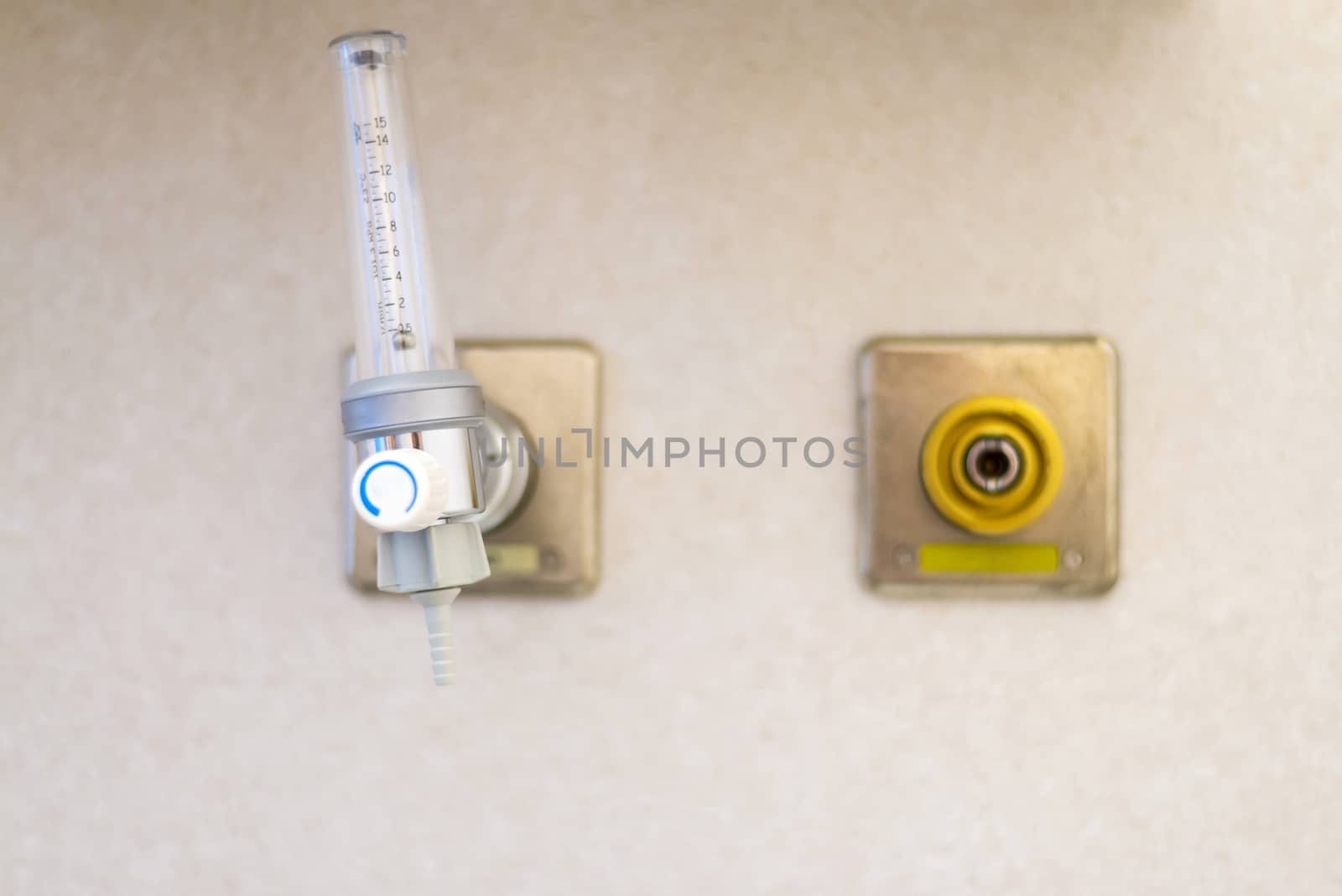 Oxygen flow meter plugged in the green outlet on white wall.