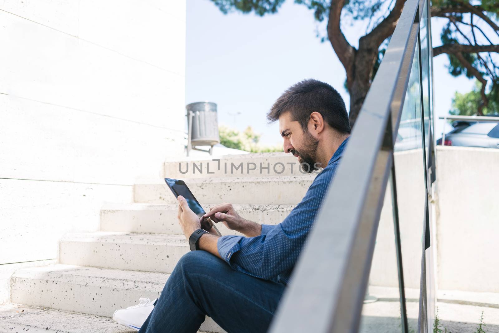 Bearded man sitting on steps while using a tablet by raferto1973