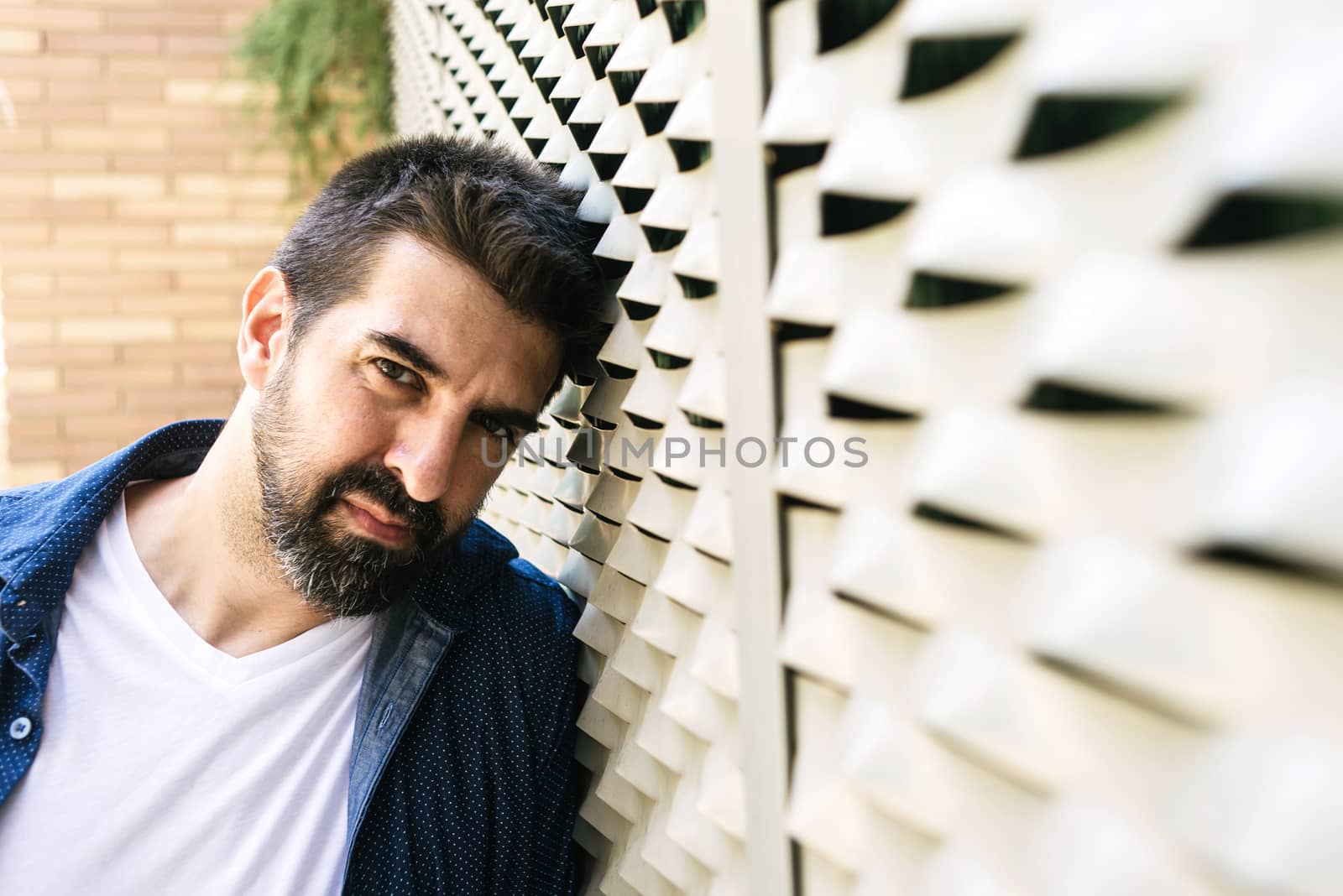 Pensive bearded male leaning on wall with hand on chin by raferto1973