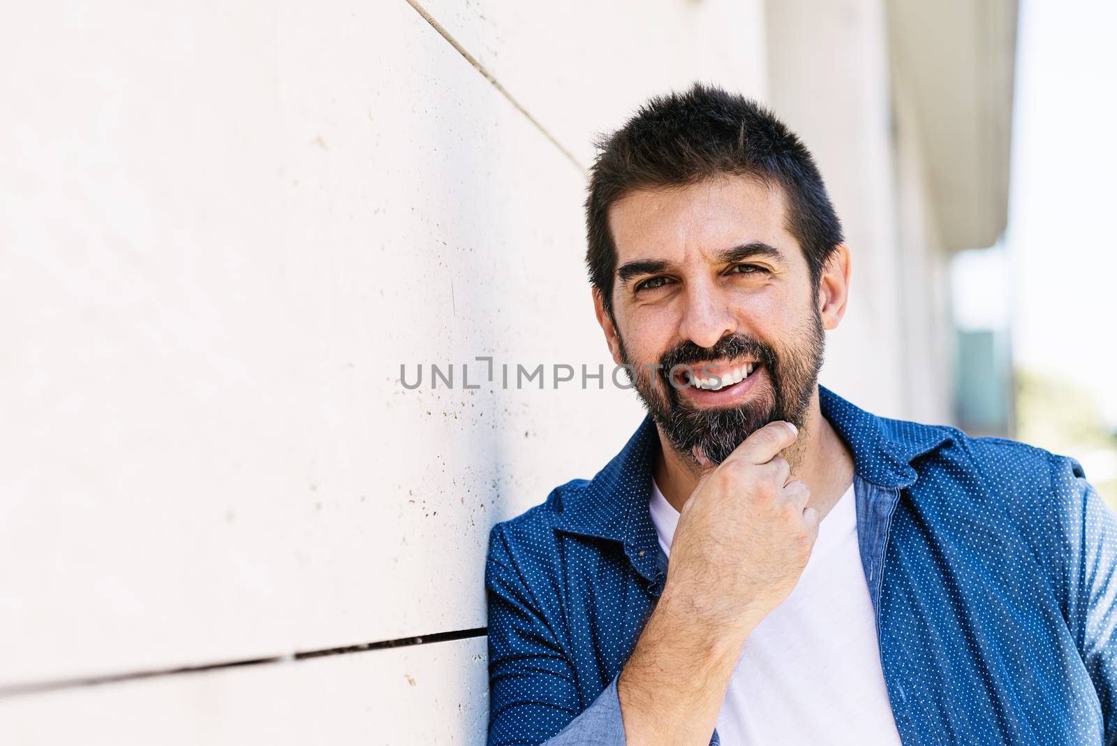 Cheerful bearded male with hand on chin while looking camera