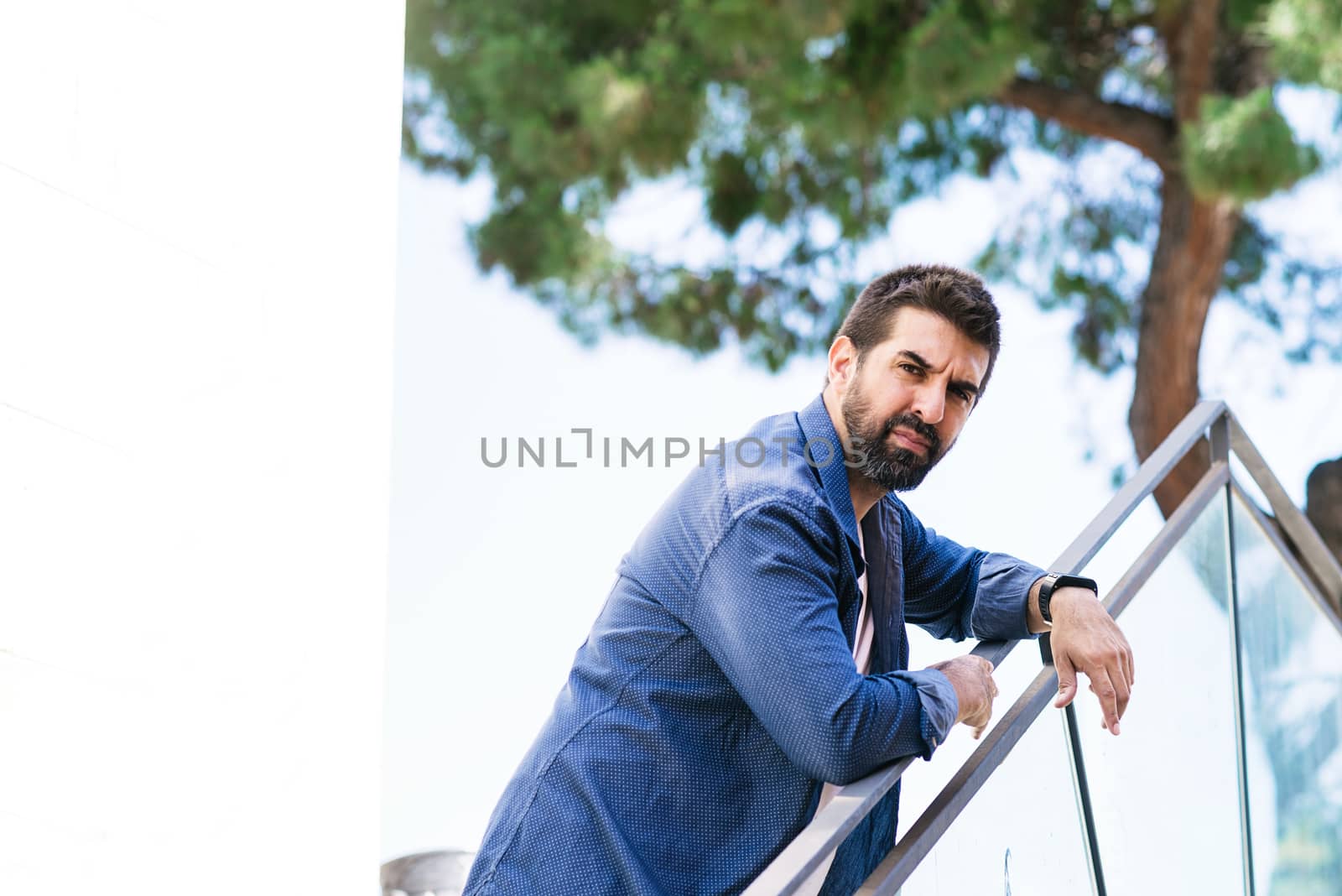 Bearded male leaning on fence while looking camera