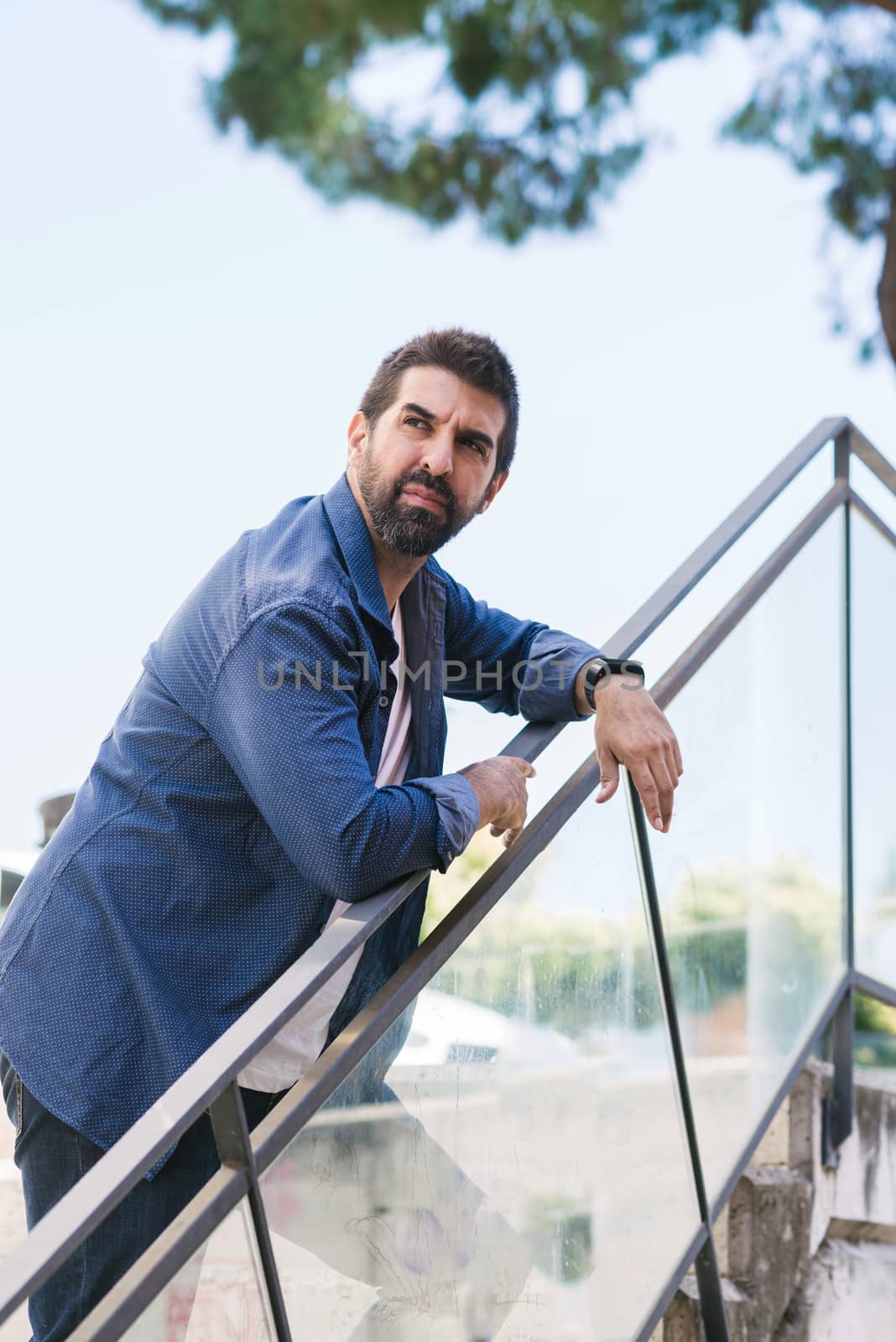 Bearded male leaning on fence while looking away