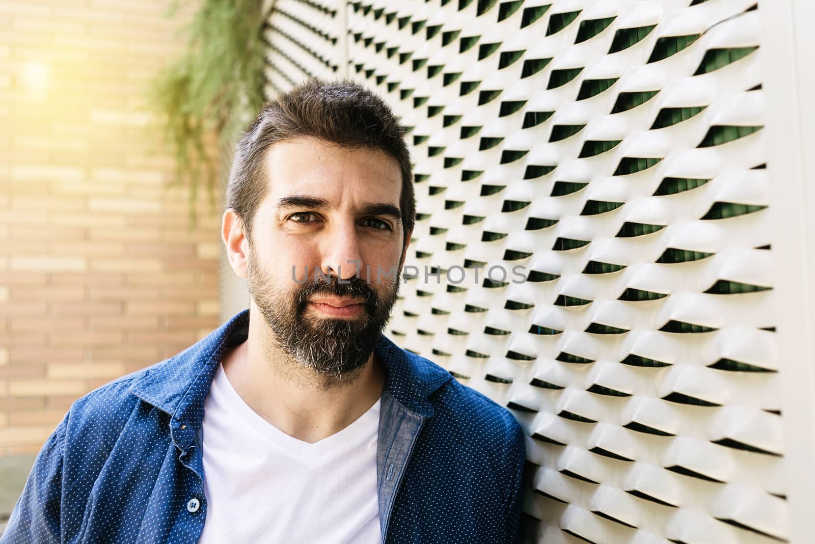 Thoughtful bearded male leaning on wall with hand on chin