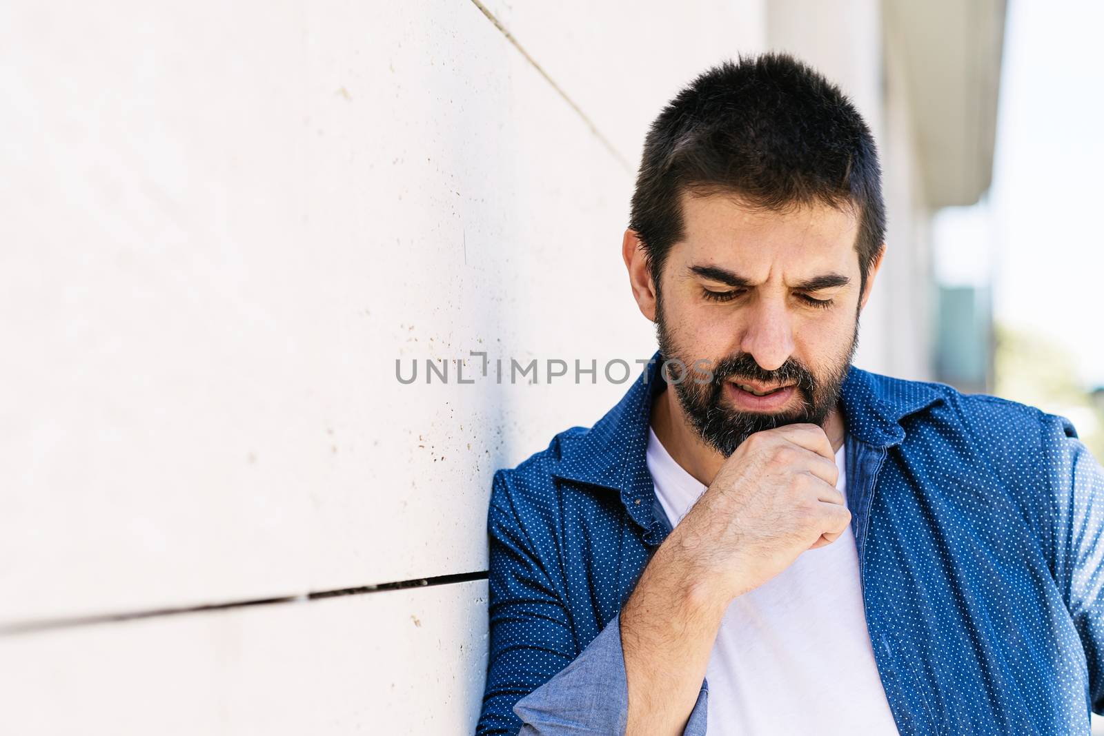 Thoughtful bearded male leaning on wall with hand on chin