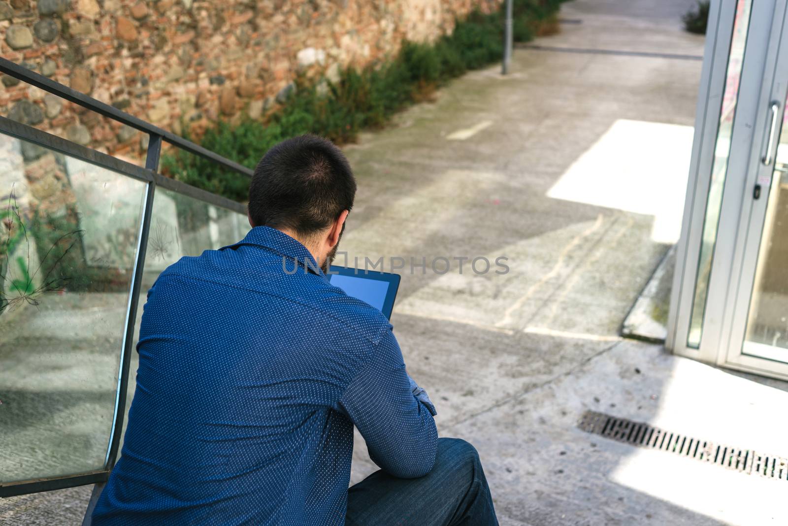 Portrait of a bearded man sitting on steps while using a tablet