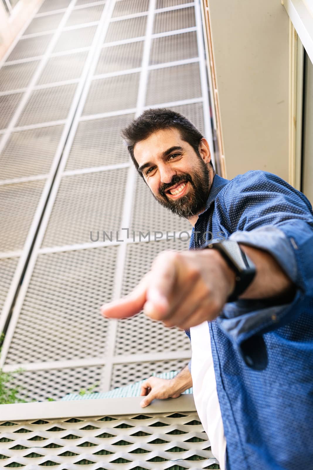 Bearded smiling male leaning on wall while pointing to you with finger