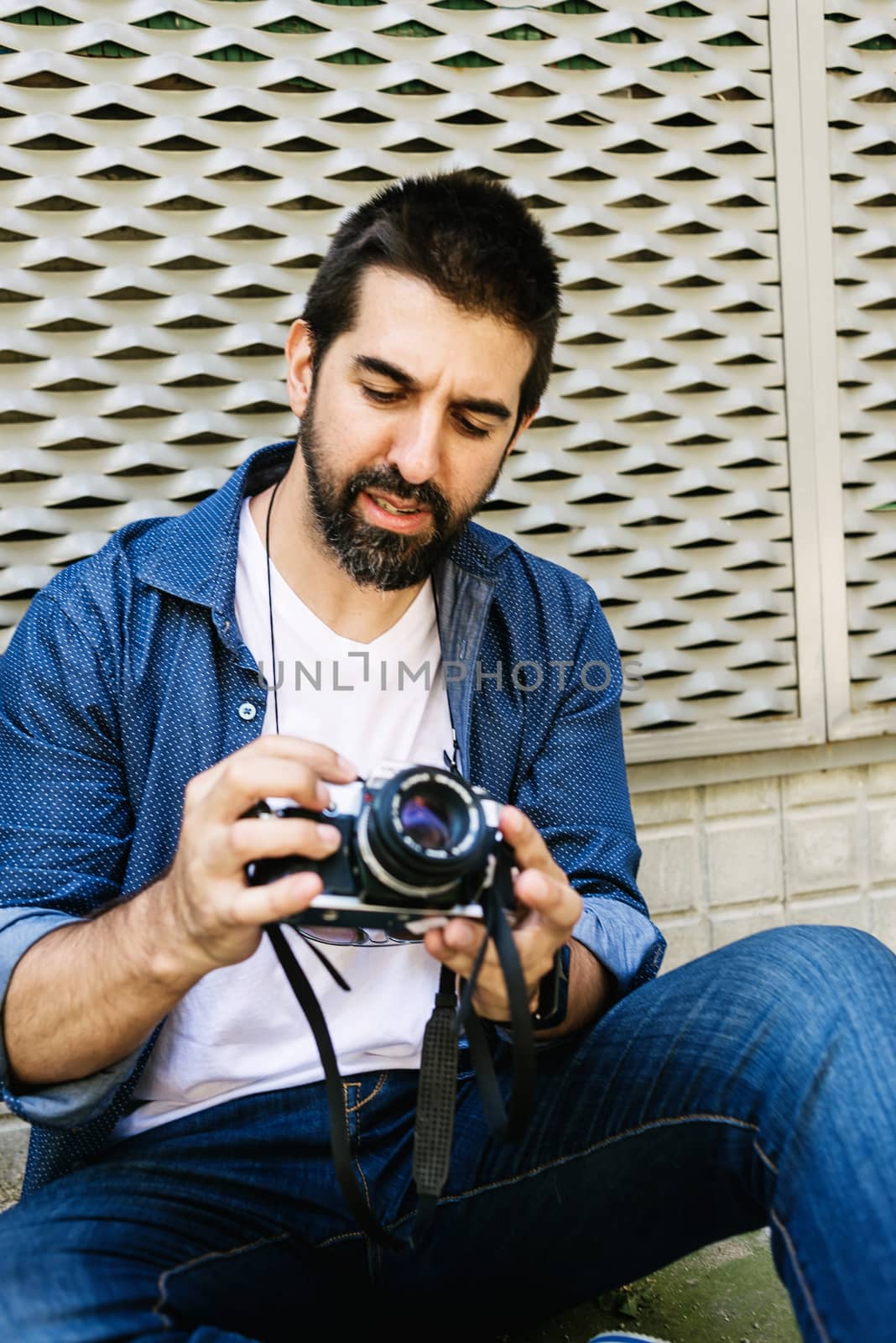 Cheerful bearded traveler man sitting on ground while using checking a camera