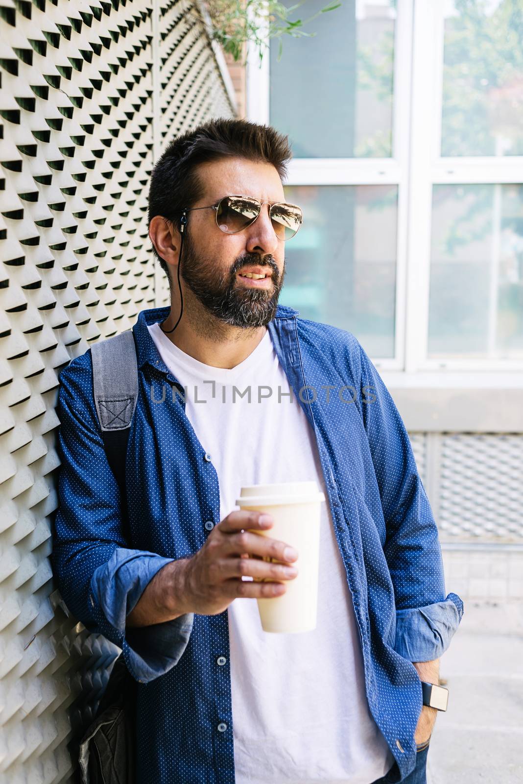 Portrait of a handsome man in blue t-shirt standing with coffee to go on a metallic wall background