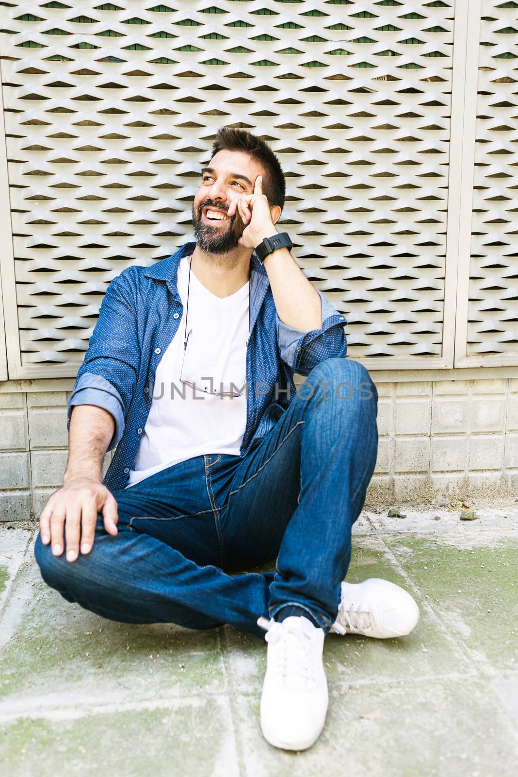Cheerful bearded man in casual attire sitting on street ground while relaxing on a coffee break