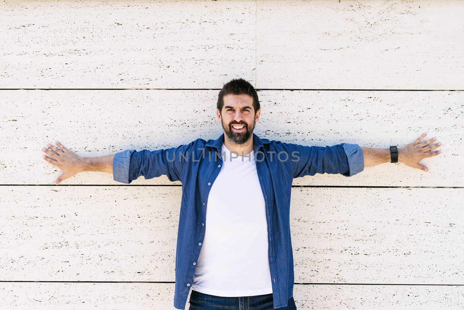 Bearded man leaning on wall with Stretched arms while looking camera with a smile
