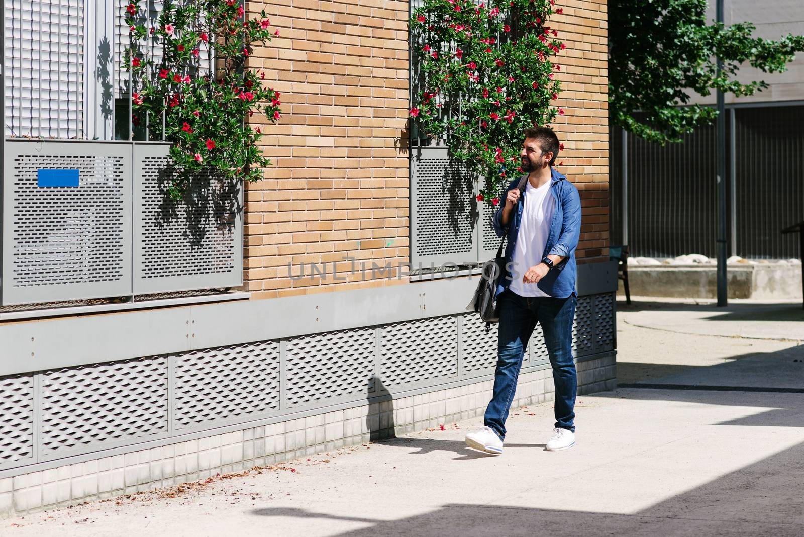 Man in casual clothes walking in the street while holding a shoulder bag