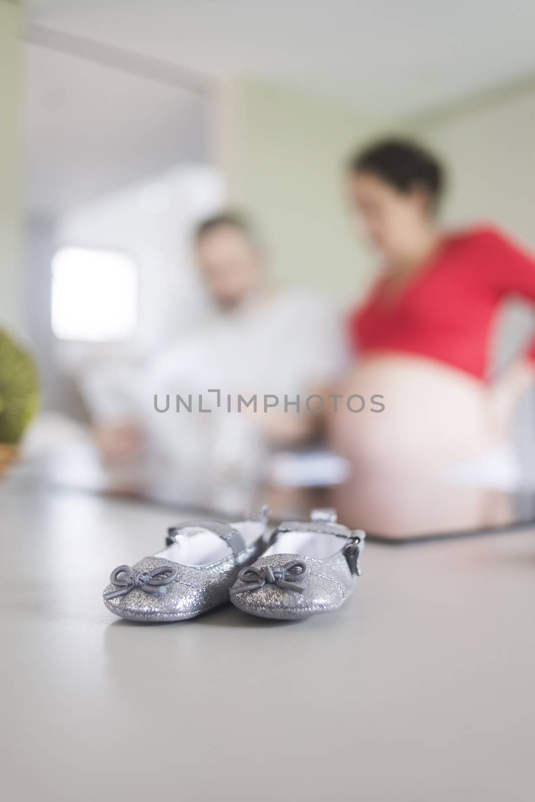 Baby shoes on a kitchen table while expecting couple standing unfocussed in the background
