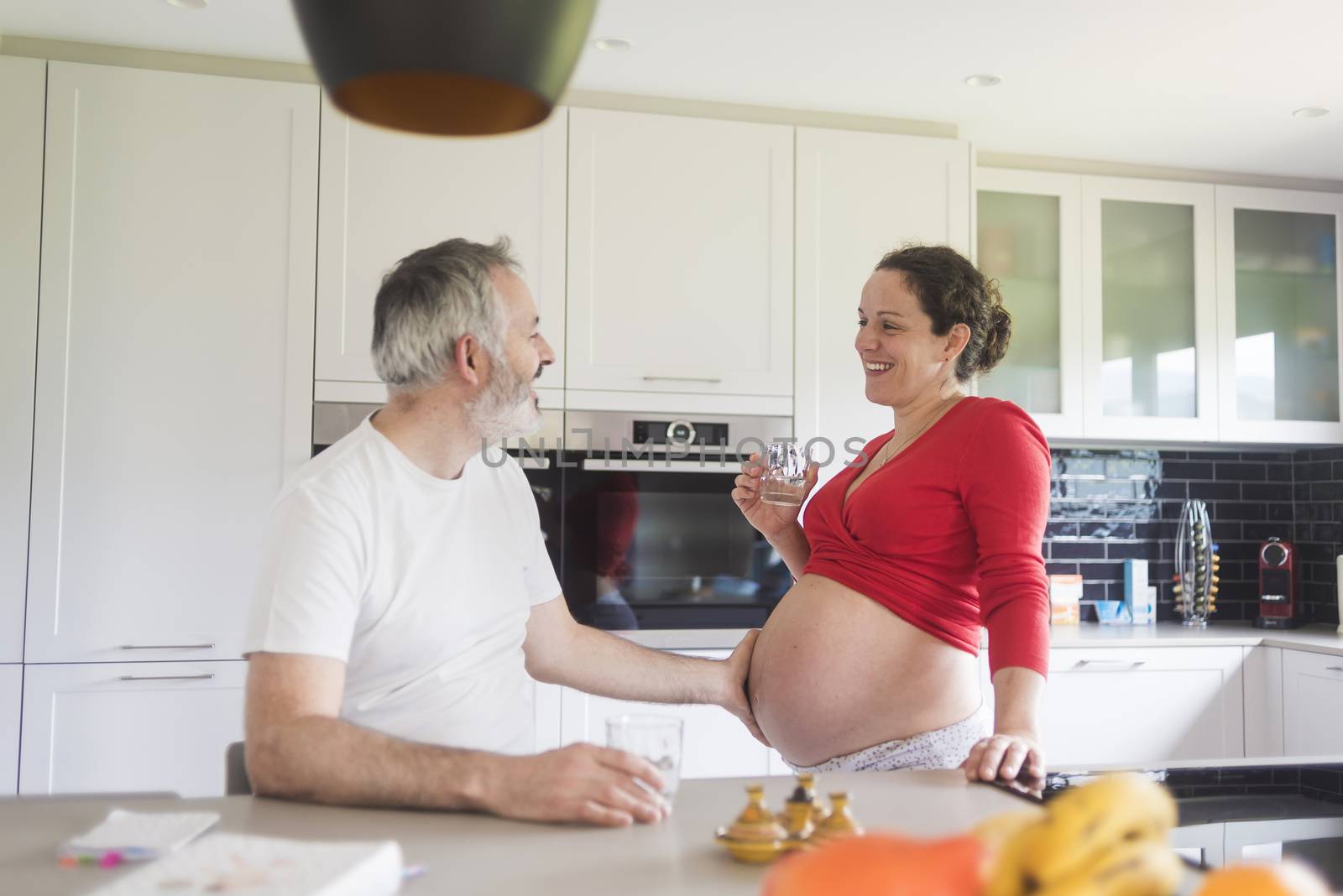 Portrait of smiling laughing white Caucasian couple two people, pregnant woman with husband in the kitchen, lifestyle healthy pregnancy happy life concept