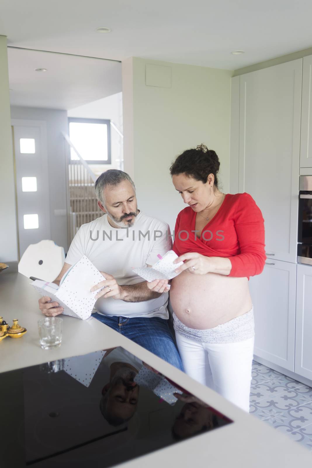 Smiling couple consulting a book at the kitchen.