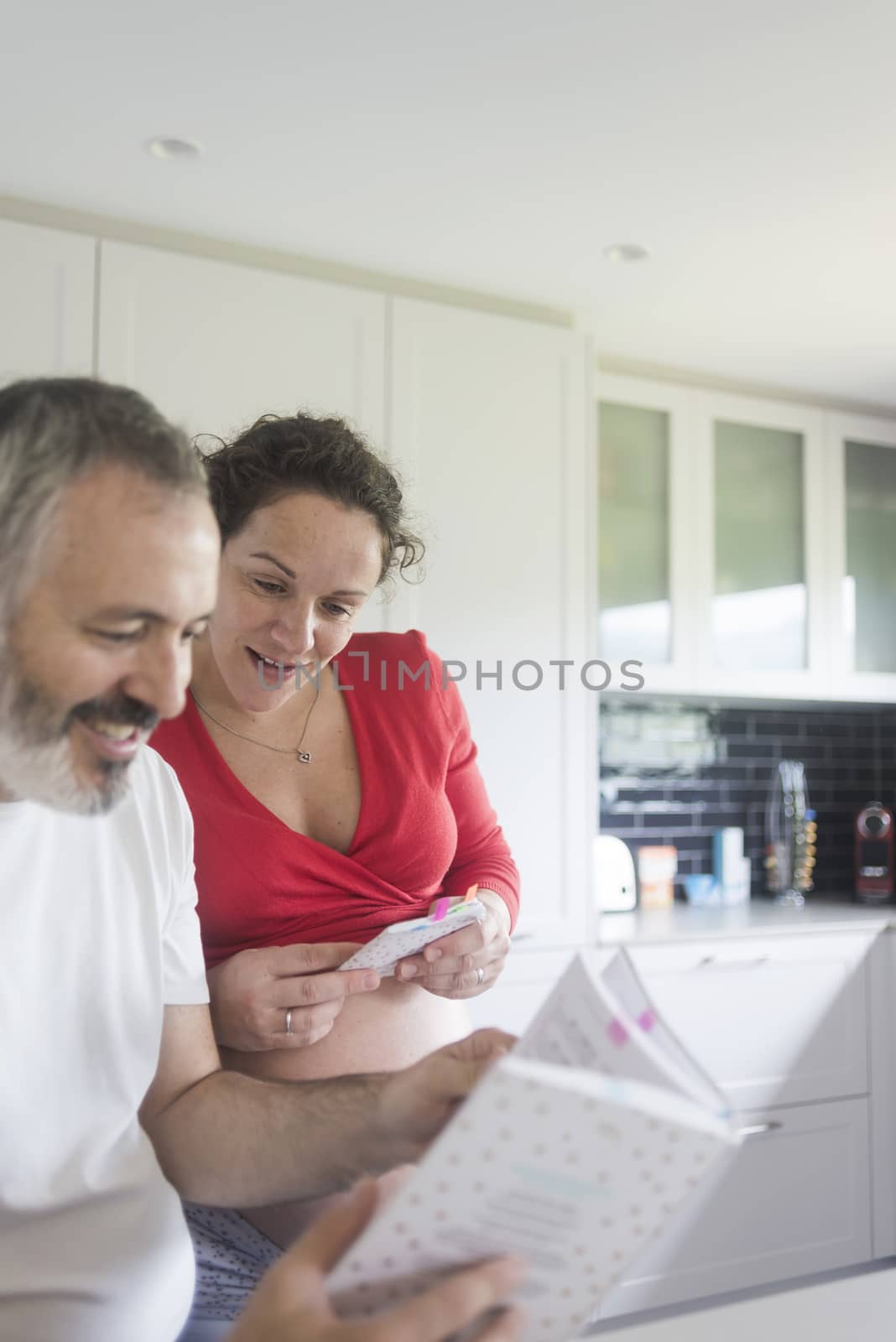 Smiling couple consulting a book at the kitchen.