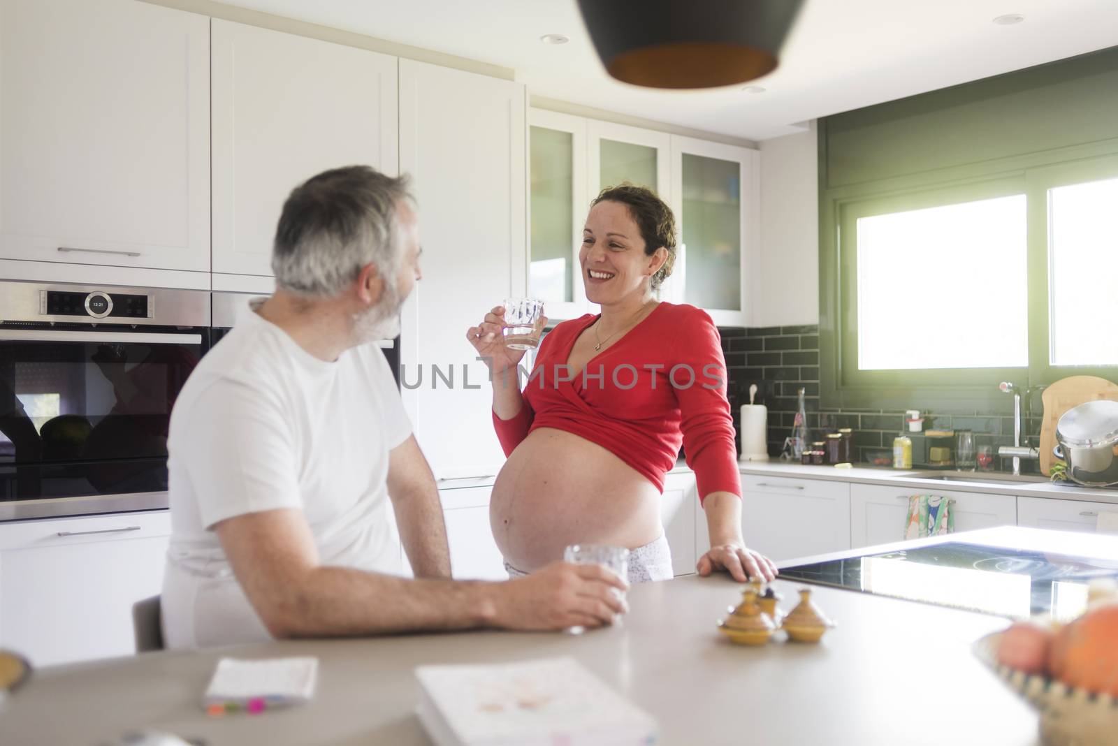Portrait of smiling laughing white Caucasian couple two people, pregnant woman with husband in the kitchen, lifestyle healthy pregnancy happy life concept