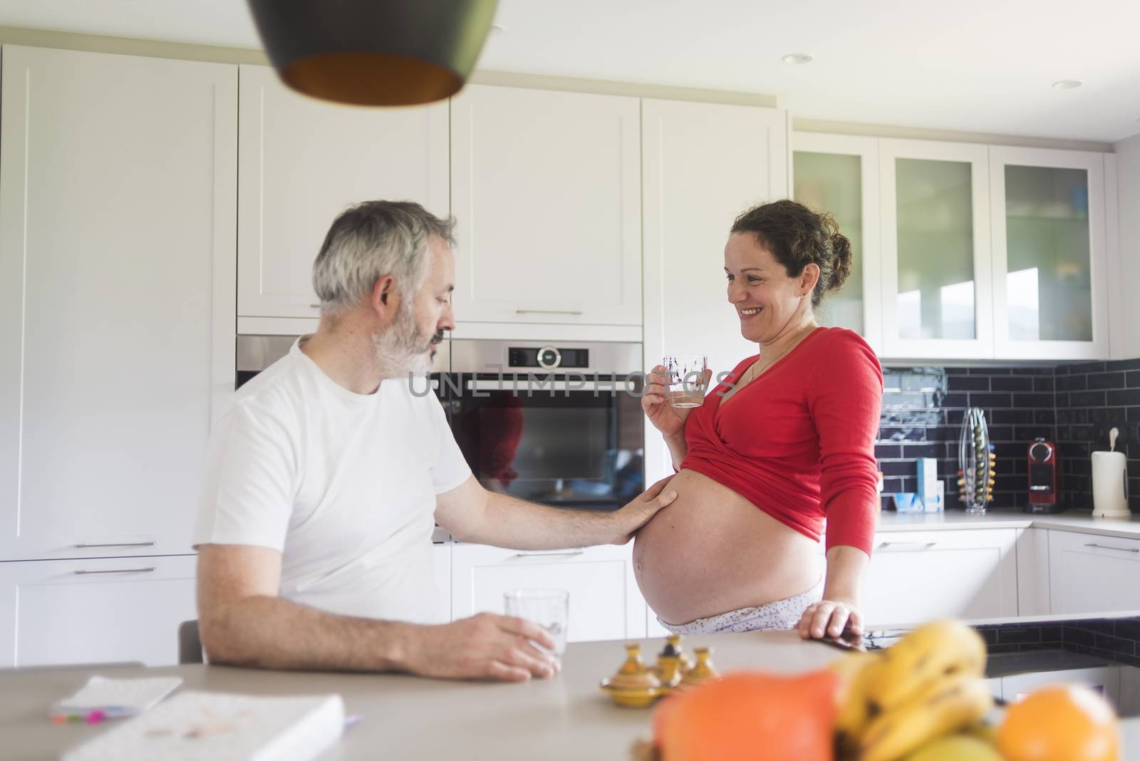 Portrait of smiling laughing white Caucasian couple two people, pregnant woman with husband in the kitchen, lifestyle healthy pregnancy happy life concept