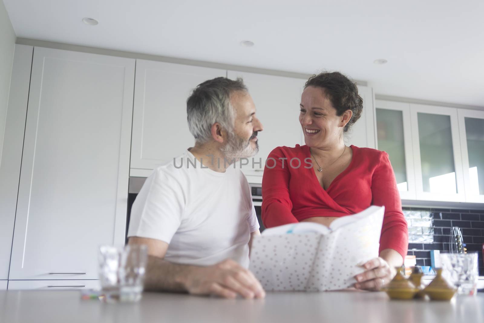 Smiling couple consulting a book at the kitchen.