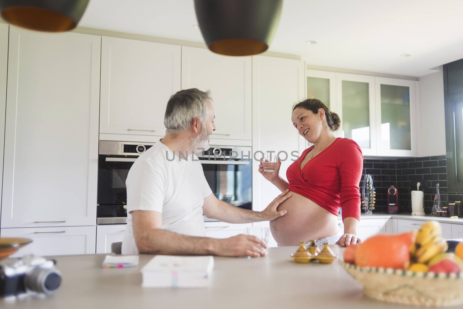 Portrait of smiling laughing white Caucasian couple two people, pregnant woman with husband in the kitchen, lifestyle healthy pregnancy happy life concept