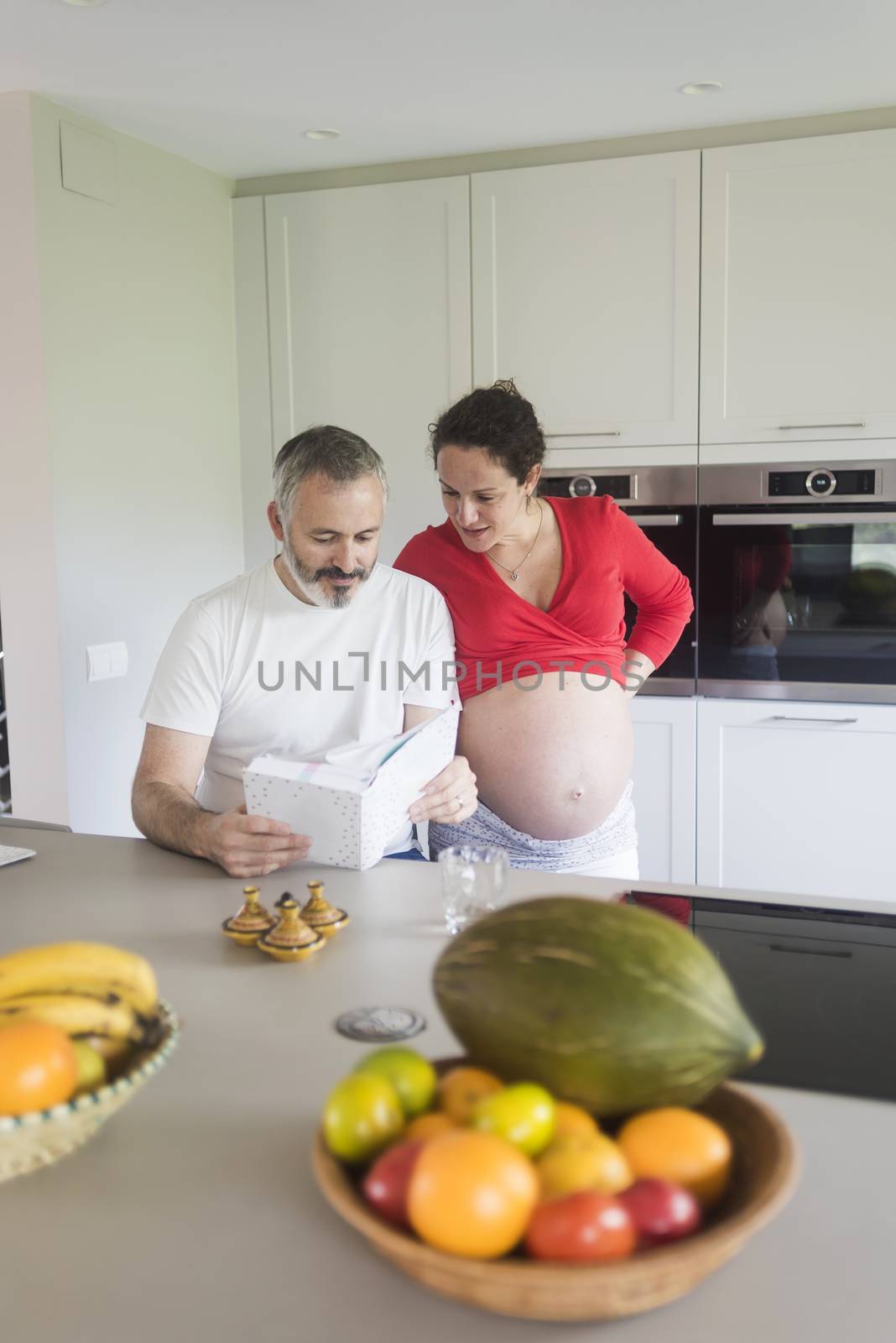 Happy pregnant woman with her husband sitting at home. Smiling couple consulting a book at the kitchen. by raferto1973
