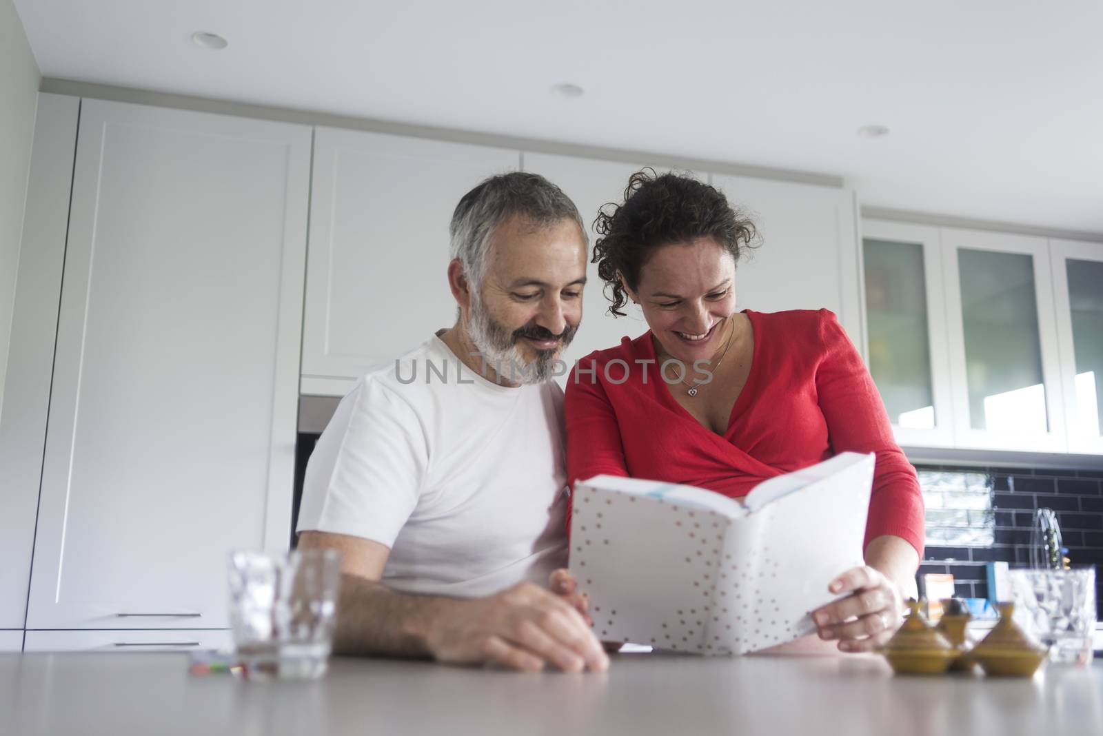 Smiling couple consulting a book at the kitchen.