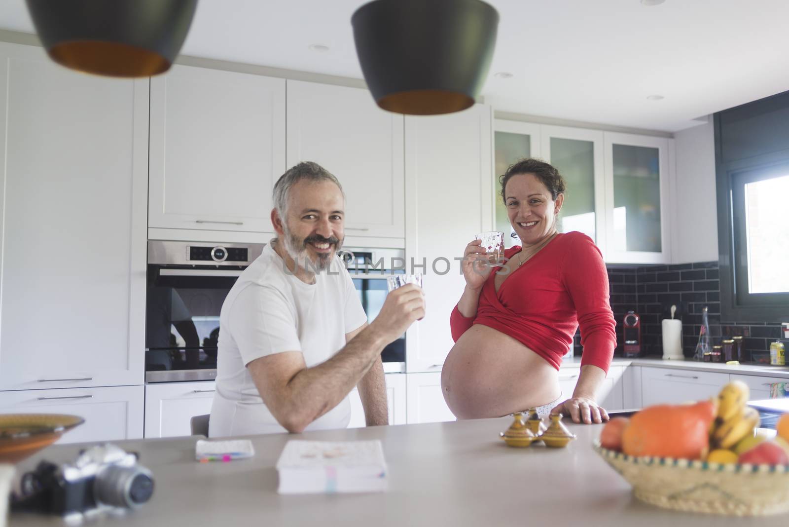 Portrait of smiling laughing white Caucasian couple two people, pregnant woman with husband in the kitchen, lifestyle healthy pregnancy happy life concept