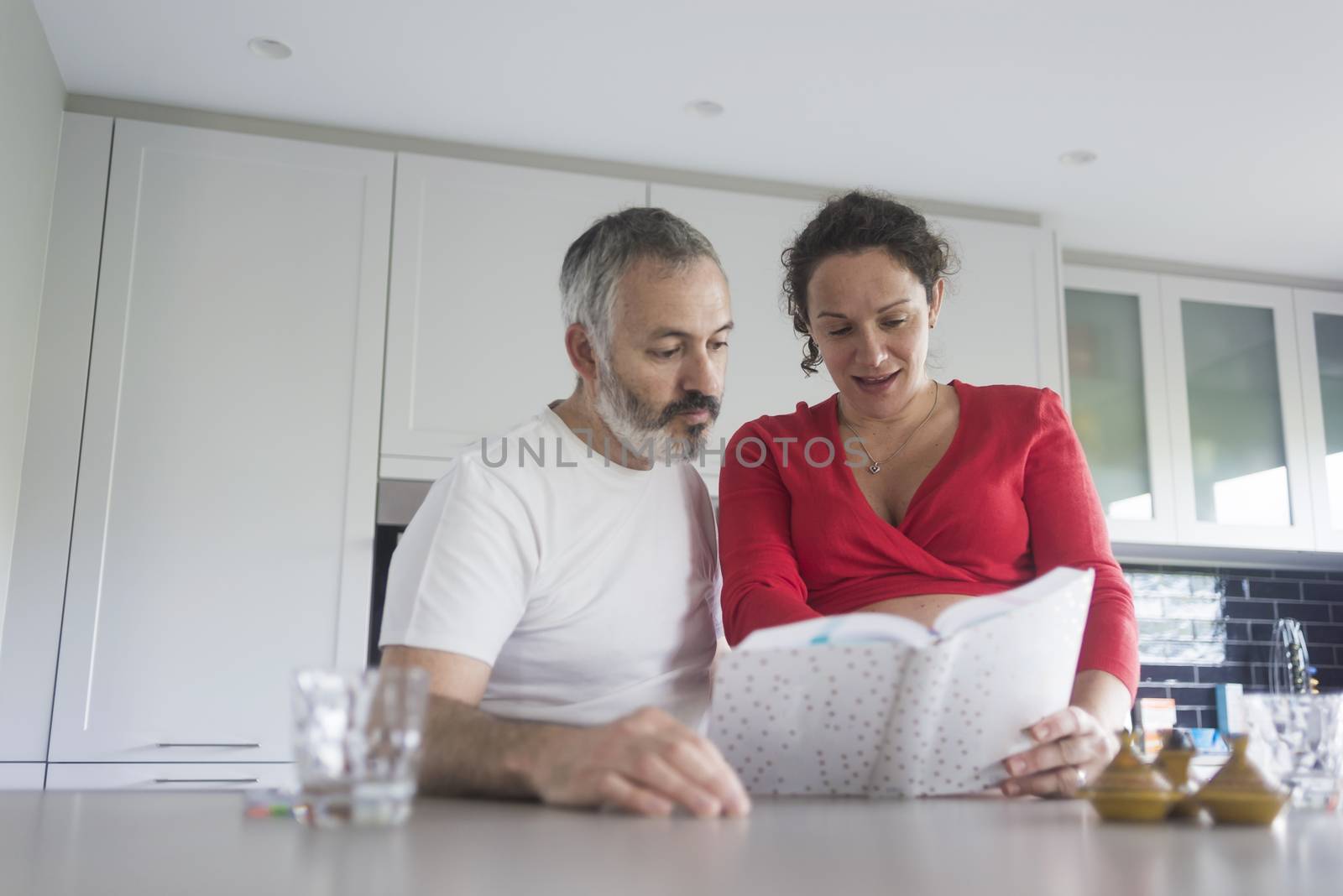 Smiling couple consulting a book at the kitchen.