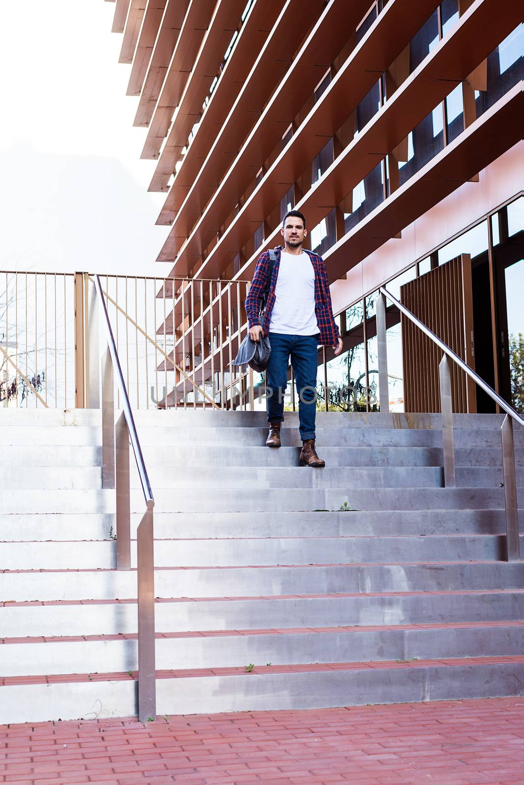 Young bearded male with shoulder bag downstairs against a business building