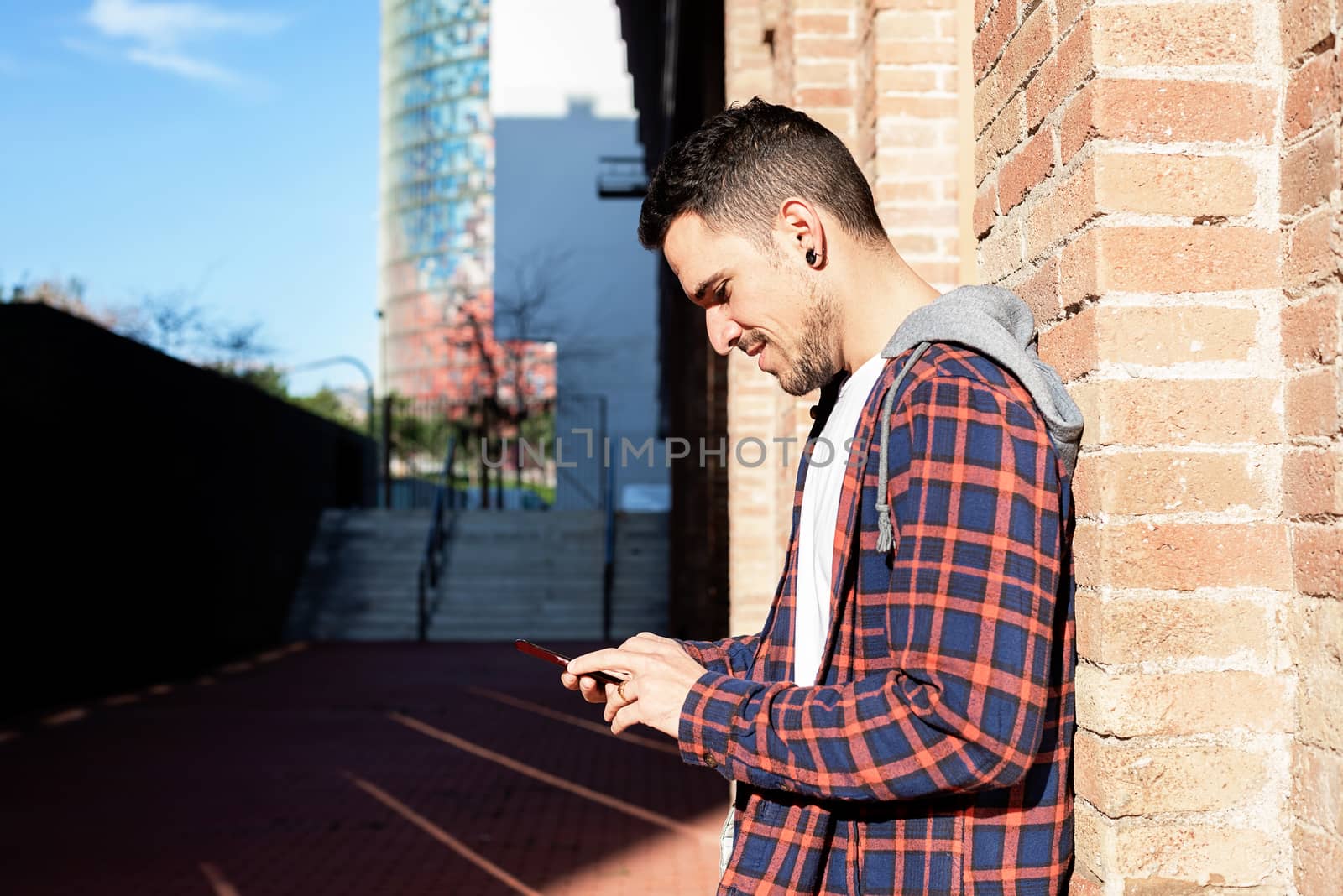 Young bearded man leaning on a bricked wall while using a smartphone