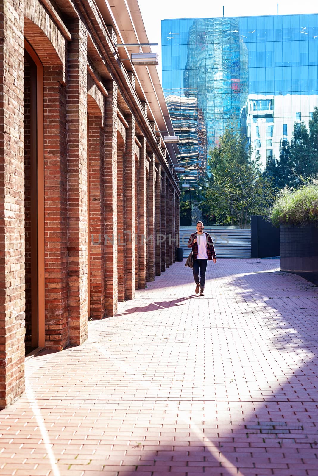 Bearded young male holding shoulder bag while walking in a business district