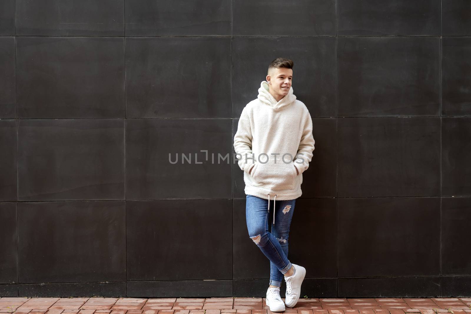 Portrait of young male with hands on pocket leaning on wall outdoors