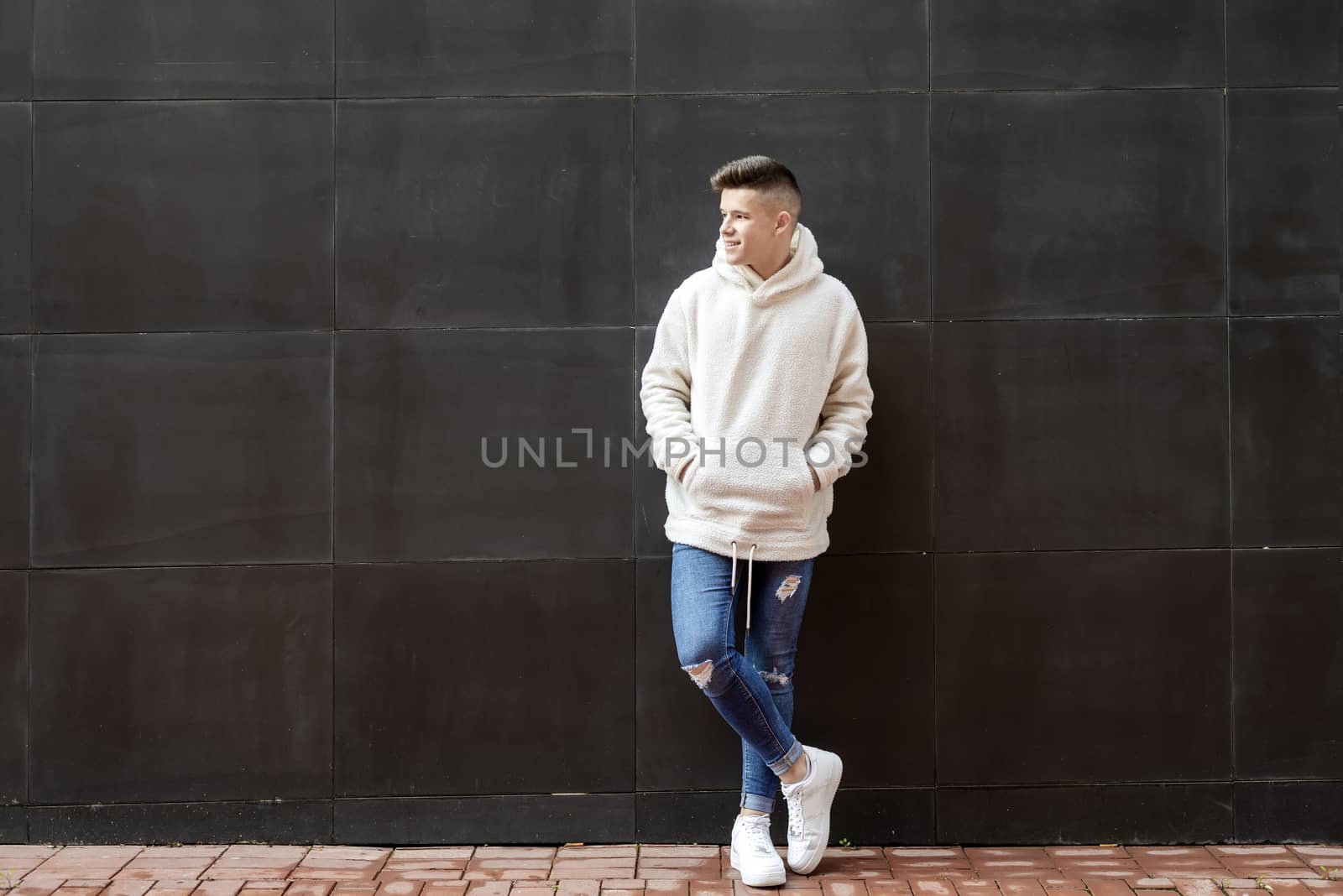 Portrait of young male with hands on pocket leaning on wall outdoors