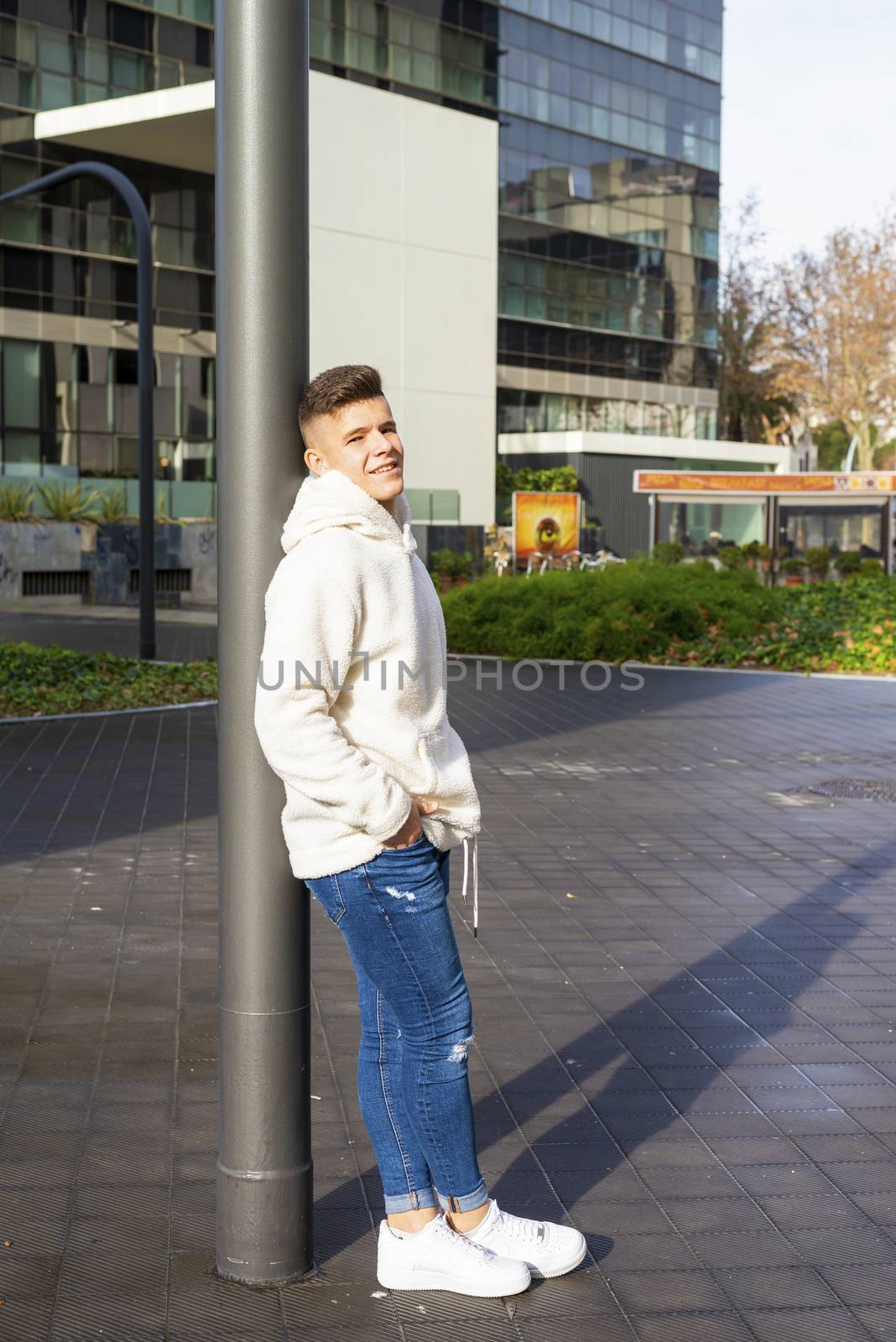 Portrait of young male with hands on pocket leaning on pole outdoors