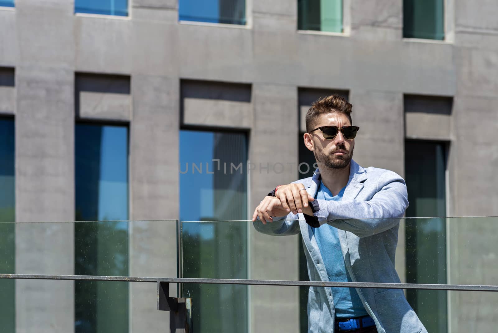 Young bearded man leaning on a fence while looking away in the city