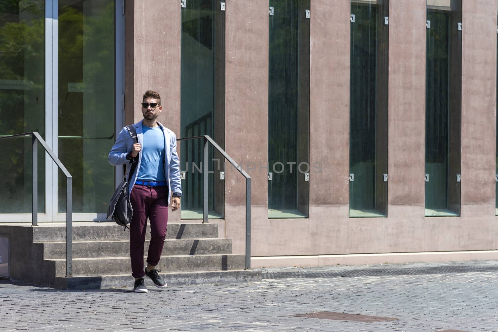 Young businessman walking next to office buildings while holding a shoulder bag outdoors