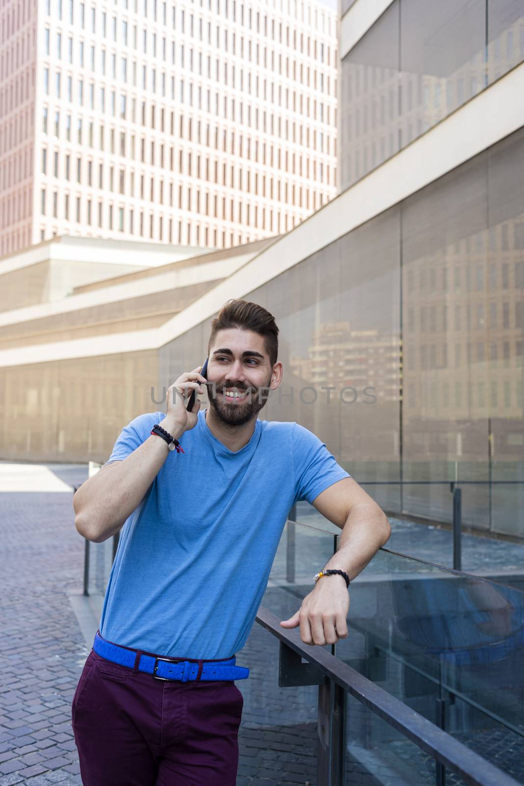 Portrait of cheerful modern businessman speaking by phone and smiling while standing outdoors