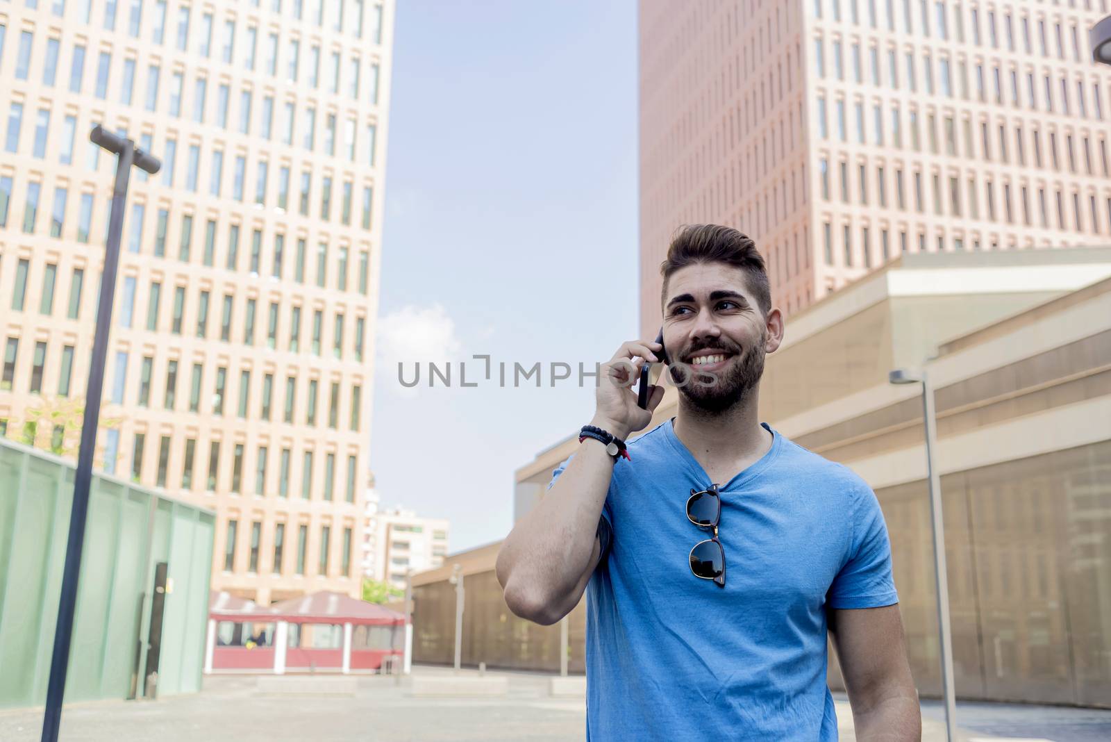 Portrait of cheerful modern businessman speaking by phone and smiling while standing outdoors