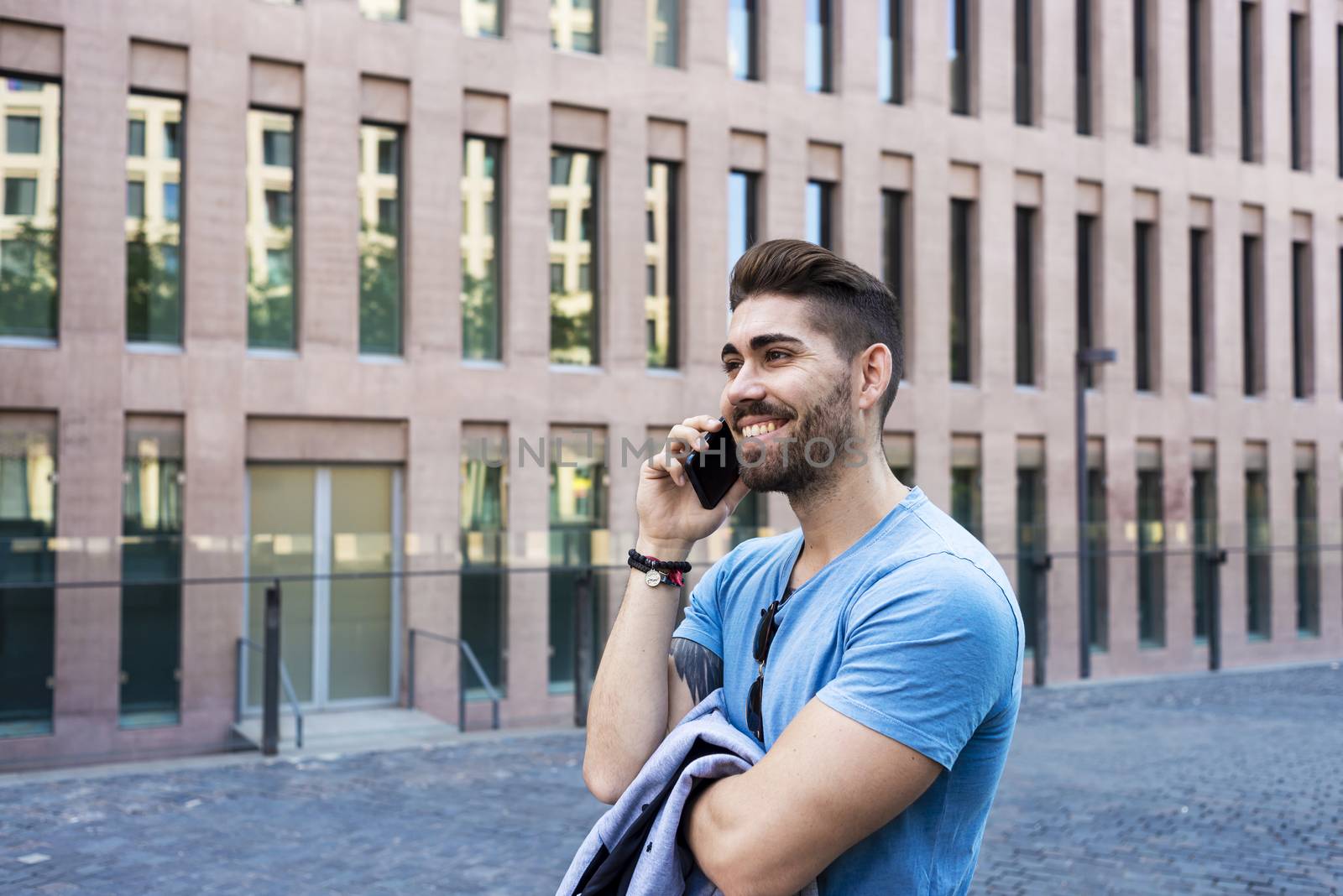 Portrait of cheerful modern businessman speaking by phone and smiling while standing outdoors