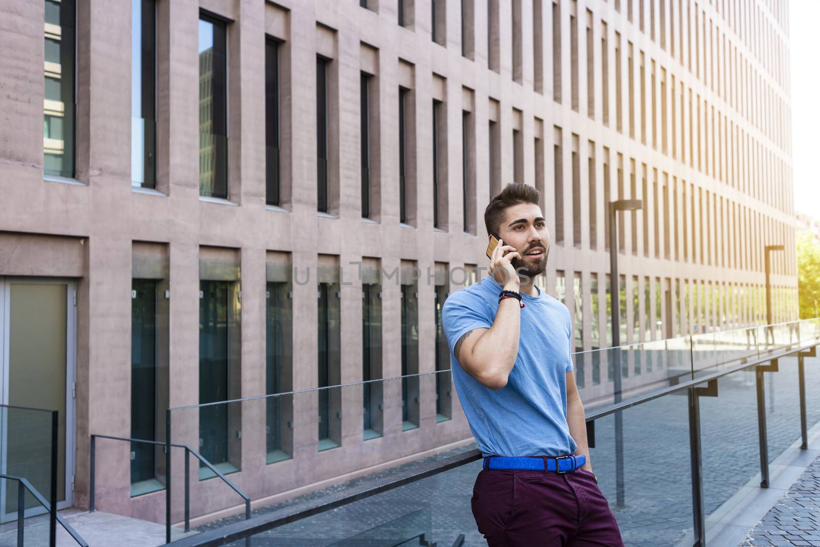 Portrait of cheerful modern businessman speaking by phone and smiling while standing outdoors