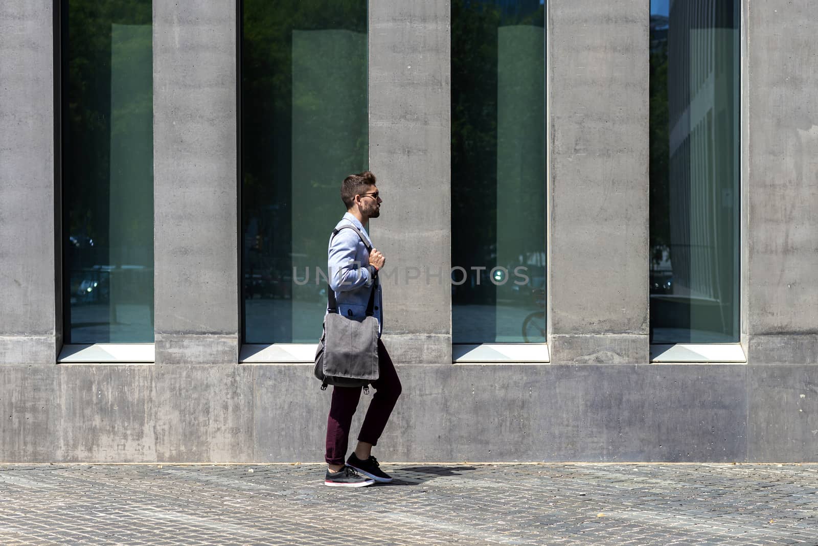 Young businessman walking next to office buildings while holding a shoulder bag outdoors